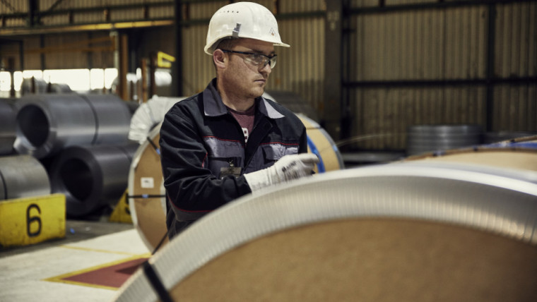 Ein Mann in einer Produktionshalle steht neben einer großen Stahlrolle.