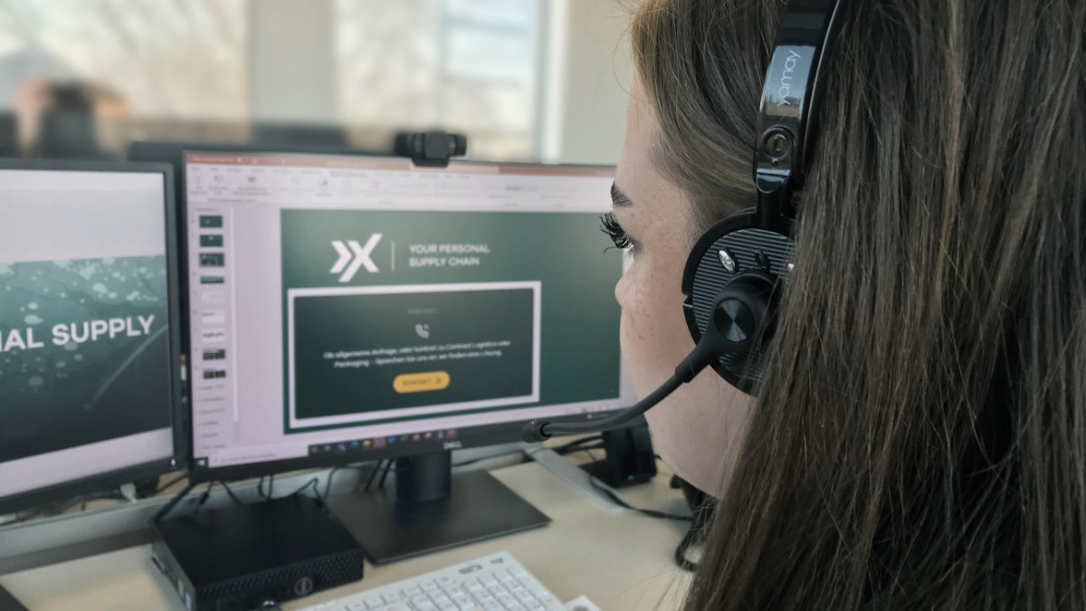 Eine AXXUM Mitarbeiterin sitzt am Schreibtisch und trägt ein Headset