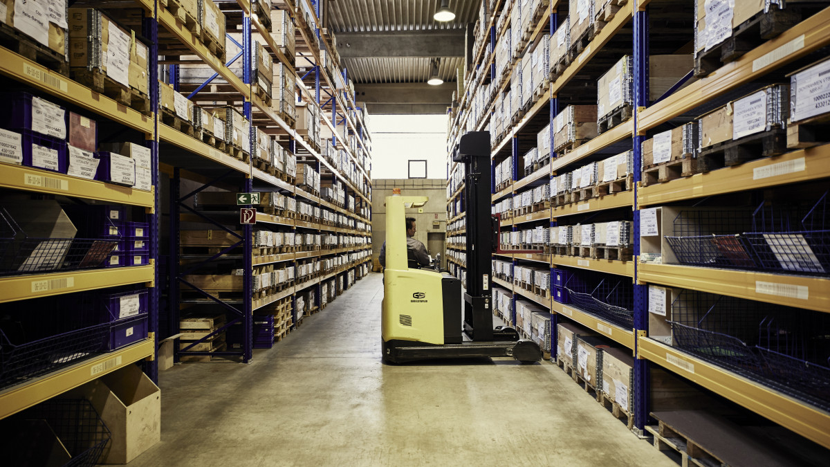 Zwischen zwei hohen Lagerregalen steht ein Gabelstapler