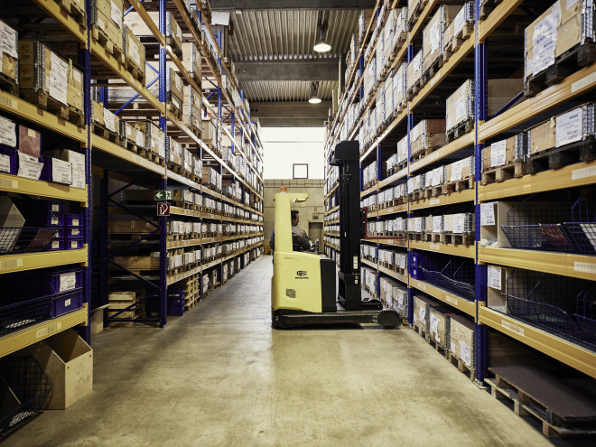Zwischen zwei hohen Lagerregalen steht ein Gabelstapler
