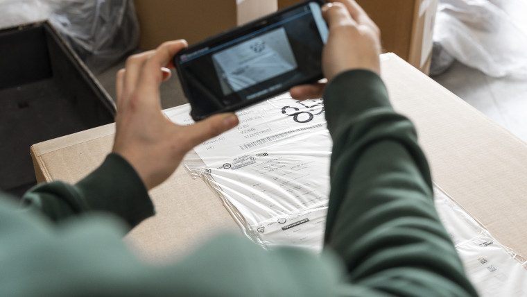 Jemand nimmt mit einem Handy eine Paketetikett auf