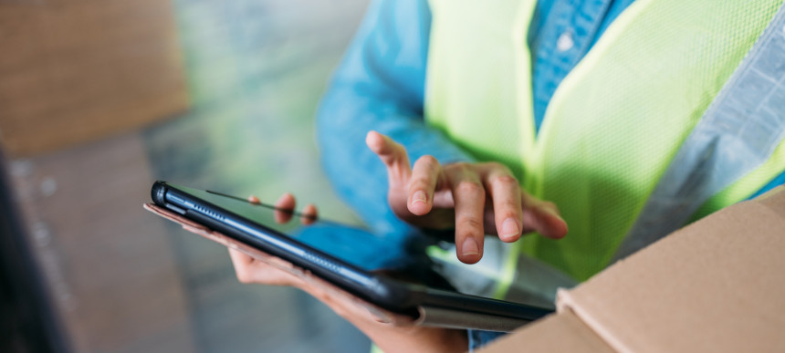 Jemand mit einer Warnweste tippt etwas auf ein Tablet ein