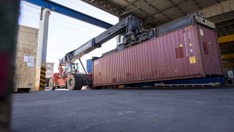 Ein großer Container wird von einem Greifstapler gegriffen.
