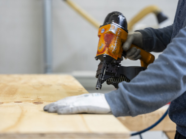 Jemand hält eine Bormaschine in der Hand und setzt zum Boren einer Holzplatte an
