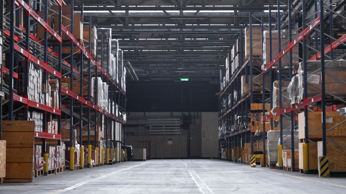 Einblick in eine große Lagerhalle. Links und rechts sind hohe Regale gefüllt mit verschiedenen Kisten