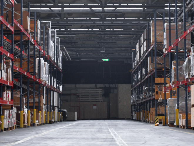 Einblick in eine große Lagerhalle. Links und rechts sind hohe Regale gefüllt mit verschiedenen Kisten