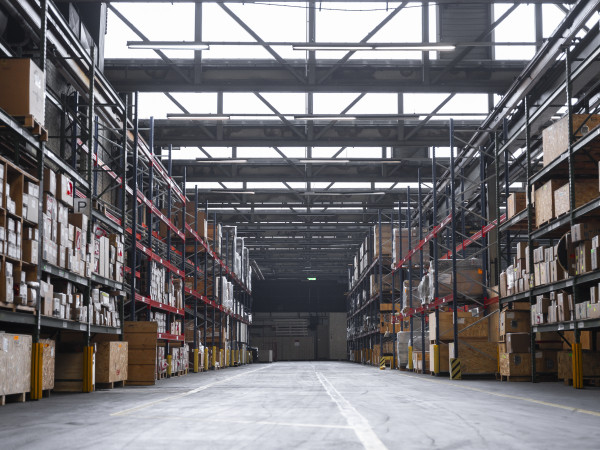 Ein Gang einer große Lagerhalle mit hohen gefüllten Regalen links und rechts