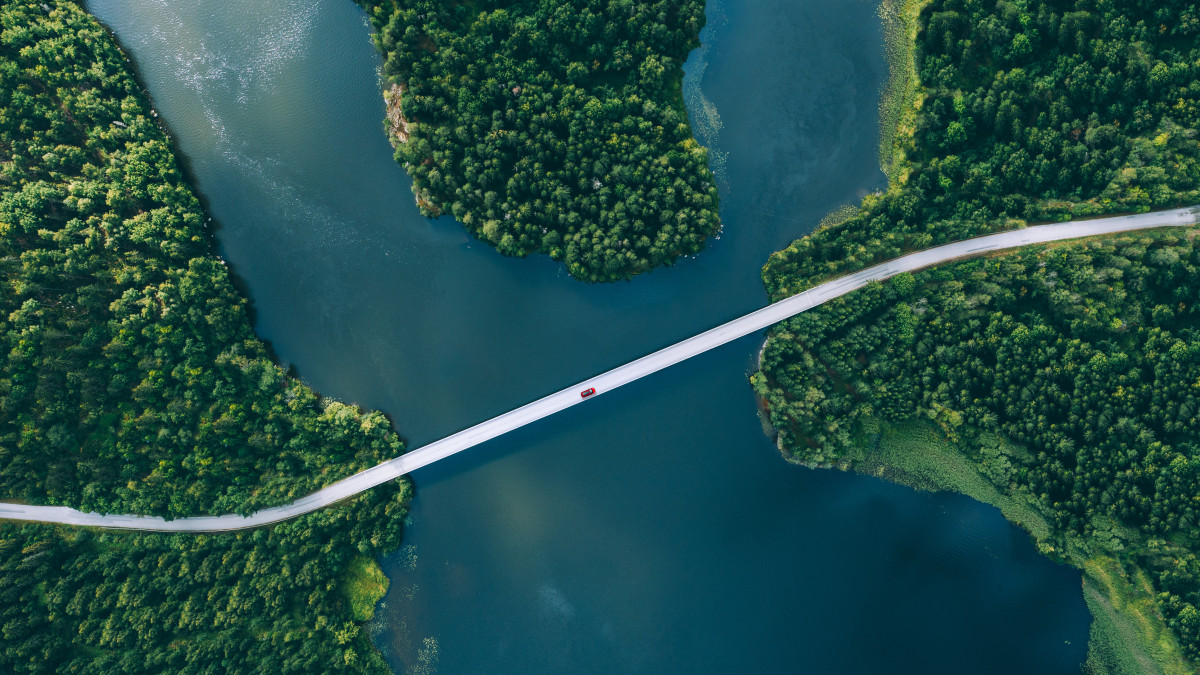 Aufnahme einer Straße aus der Vogelperspektive, die durch einen Wald und über einen Fluss führt.