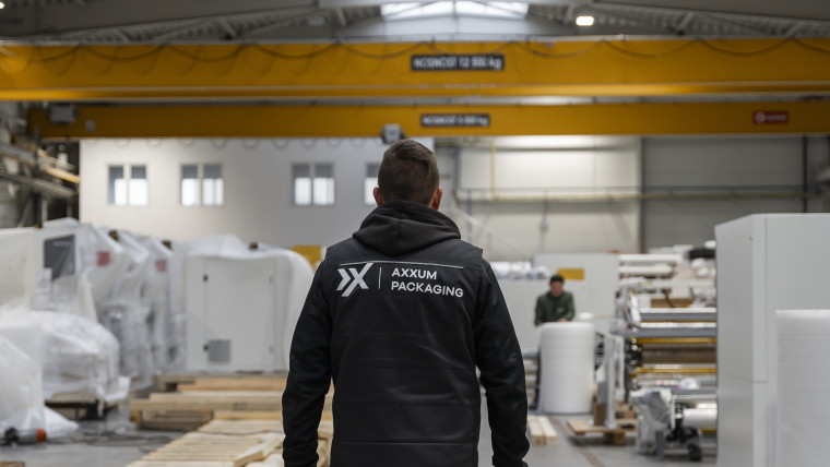 Ein Mann trägt eine schwarze AXXUM-Jacke und steht in einer industriellen Umgebung.