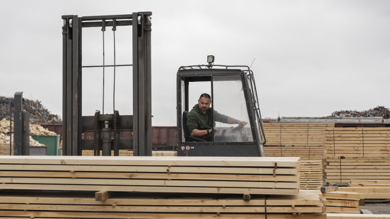 Ein Mann steuert einen Gabelstapler, während er vor gestapeltem Holz steht.