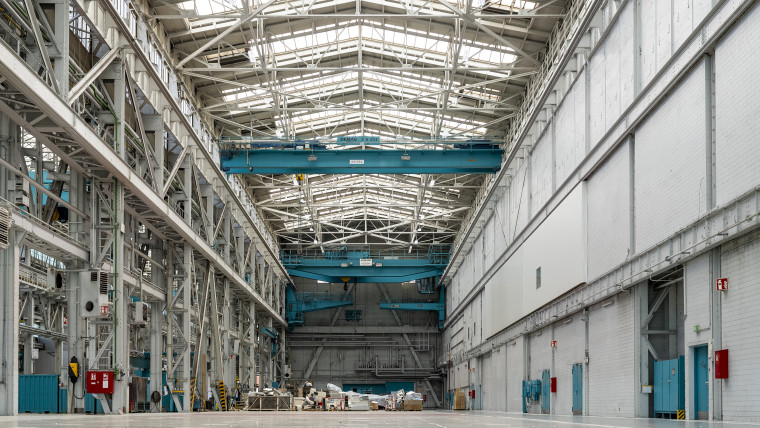 Innenansicht eines leeren Lagerhauses, das von einem großen Metalldach überspannt wird.