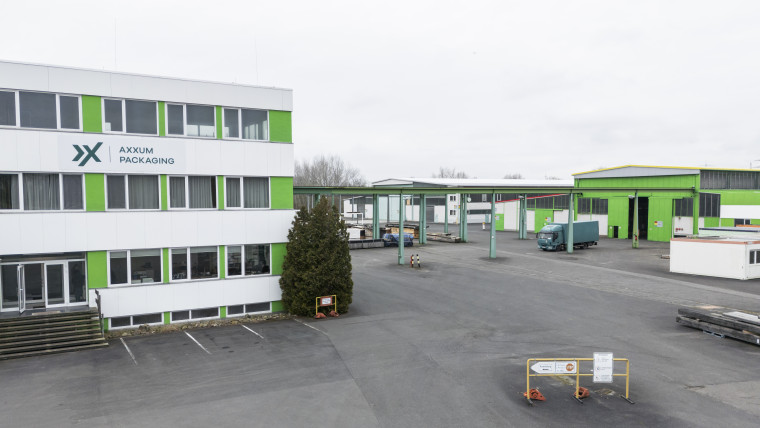 Betriebsgelände von AXXUM Packaging Hessen mit mehrstöckigem Bürogebäude links und mehreren Lagerhallen rechts