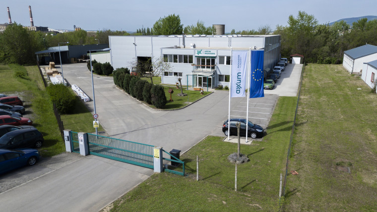 Übersichtliche Luftaufnahme einer Fabrik mit Autos, die davor geparkt sind.