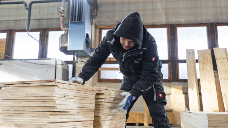 Ein Mann mit schwarzem Hoodie bearbeitet einen Stapel Holz.