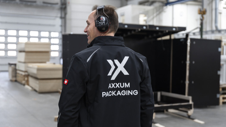Ein Mann mit einer schwarzen AXXUM-Packaging Jacke steht in einer Lagerhalle