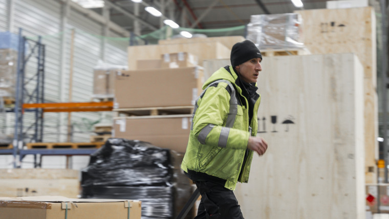 Ein Mann in einer gelben Jacke geht durch ein Lagerhaus.