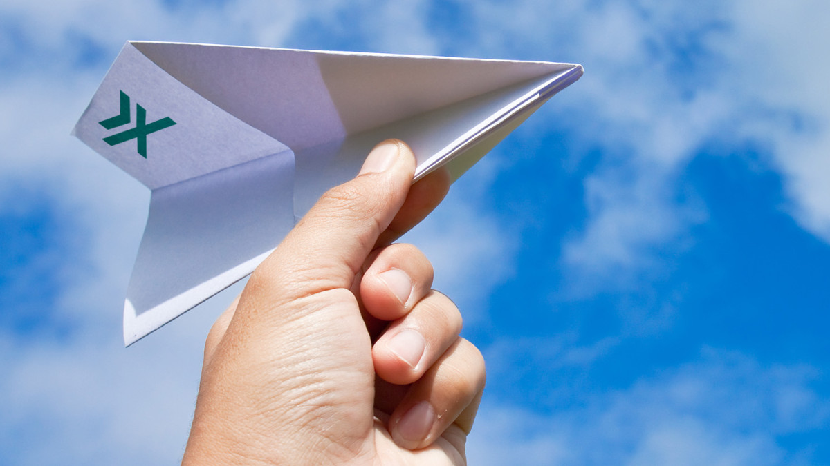 Hand hält Papierflieger mit grünem Logo vor blauem Himmel